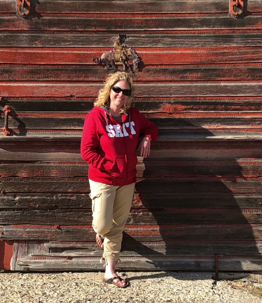 Blonde girl in front of weathered, red barn door in Saskatchewan