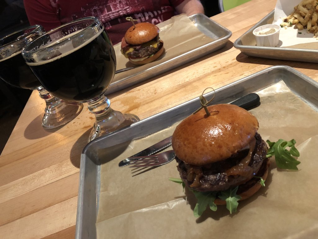 Two dark porter beers and two burgers with arugula and carmelized onions served on a brioche bun.
