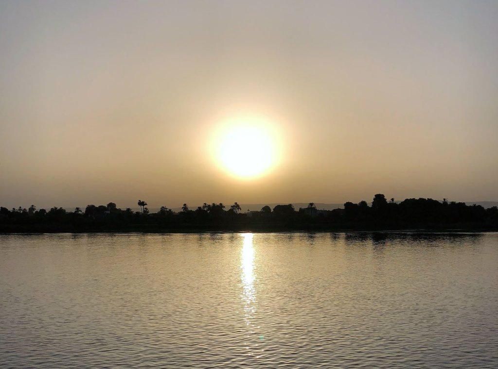 Sunset on the Nile River in Egypt. Large sun is setting over palm trees and the water. The water is calm and the trees are outlined in a silouhette of themselves.
