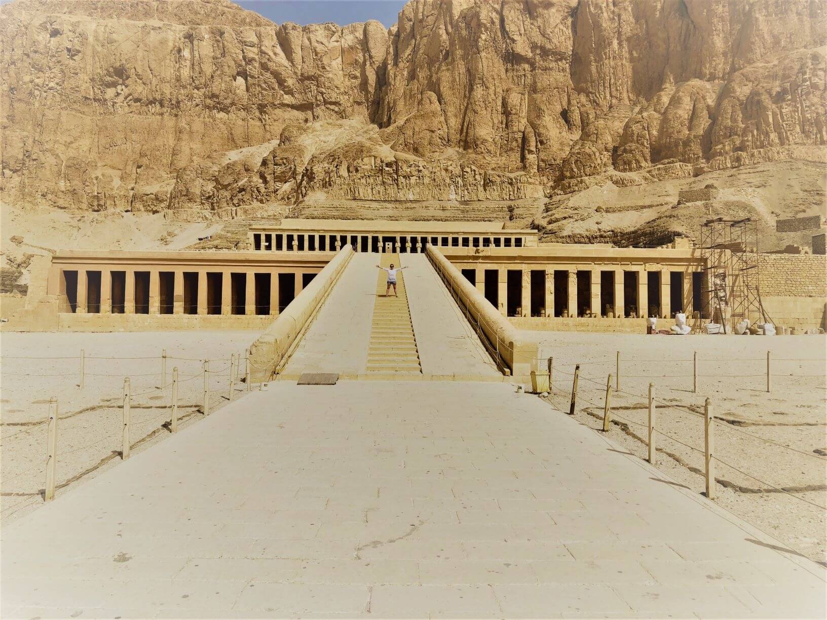 A lady stands on the stairway leading up to Queen Hatshepsut's Palace with arms outspread.