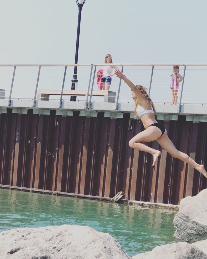 Girl jumping off rocks into the water near a pier