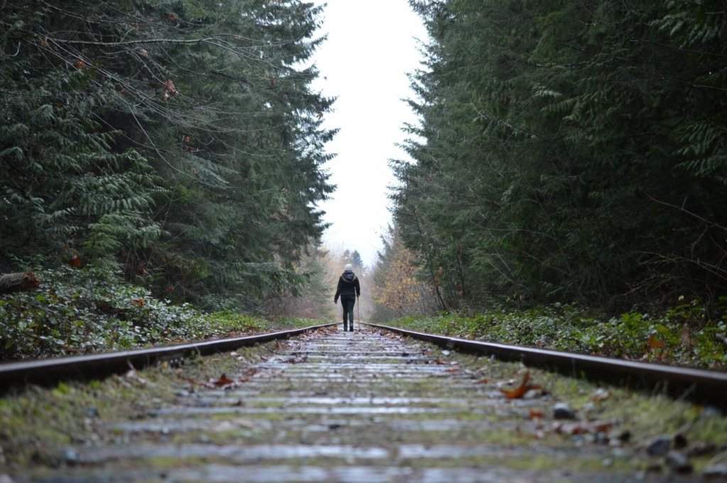 Girl walking along railway tracks with pine trees on each side in Qualicum Beach, Canada