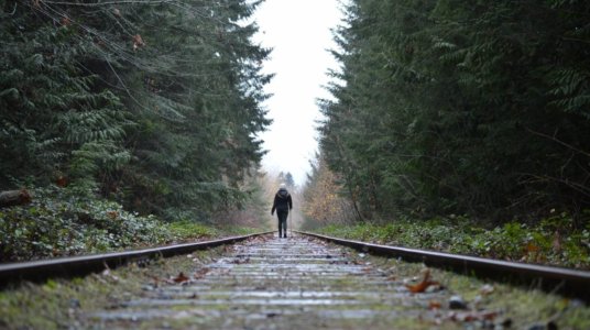 Girl walking along railway tracks with pine trees on each side in Qualicum Beach, Canada