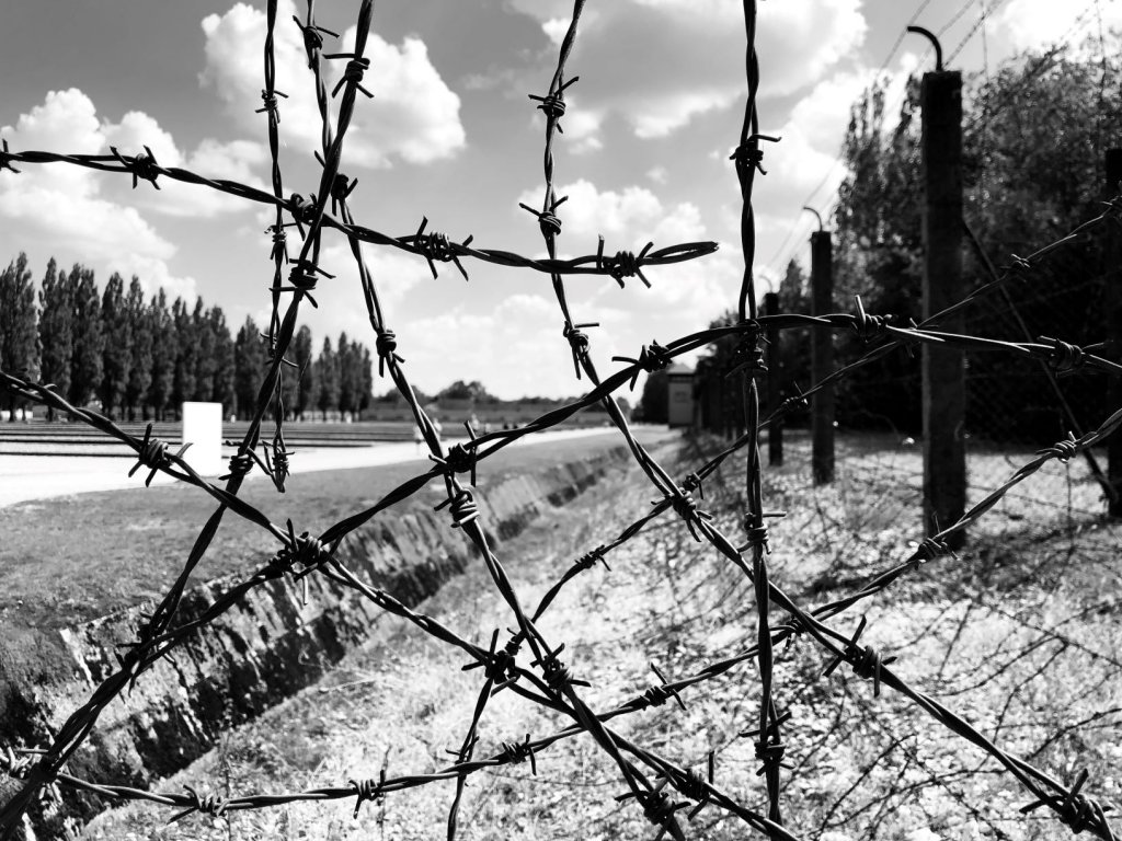 Barbed Wire fence at Dachau Concentration Camp with views of the ditch and watchtower seen through the fence.