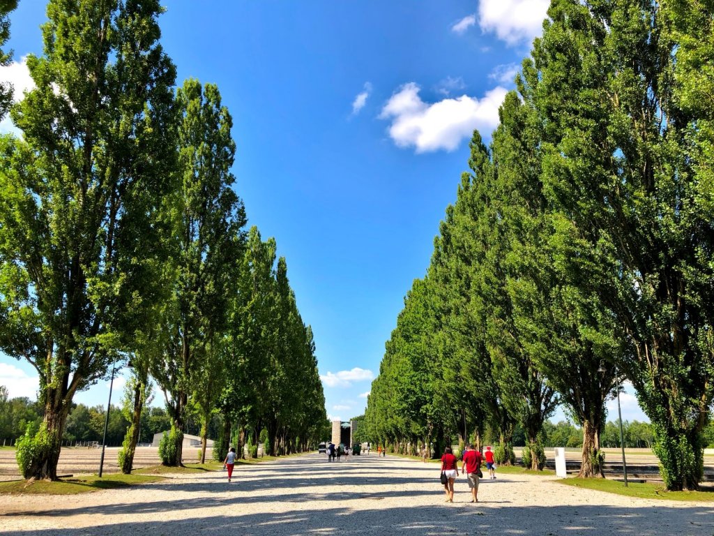 Trees line a gravel road inside Dachau Concentration Camp. The Catholic Memorial is in the distance.