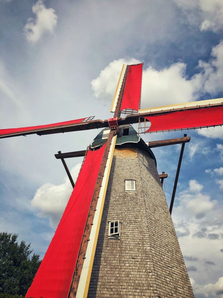 Large windmill with red banners stands against a blue sky with clouds in Bokrijk, Belgium