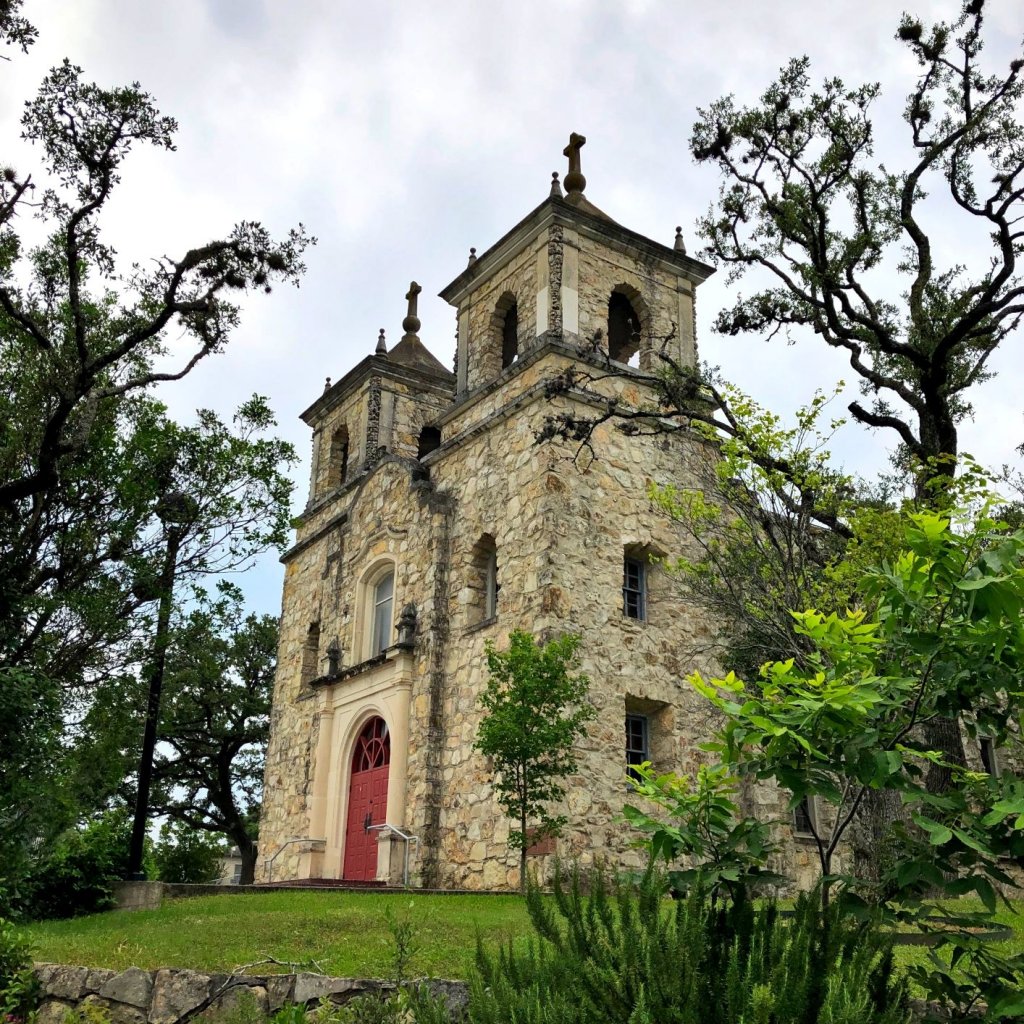 large, stone church with red door surrounded by trees and greenery