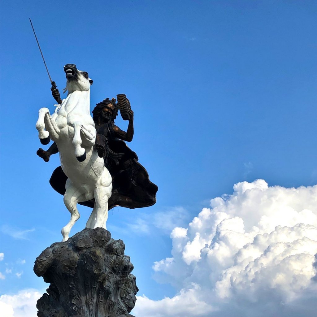 Bronze statue of Jesus sits atop a white stallion holding a sword with clouds in the background