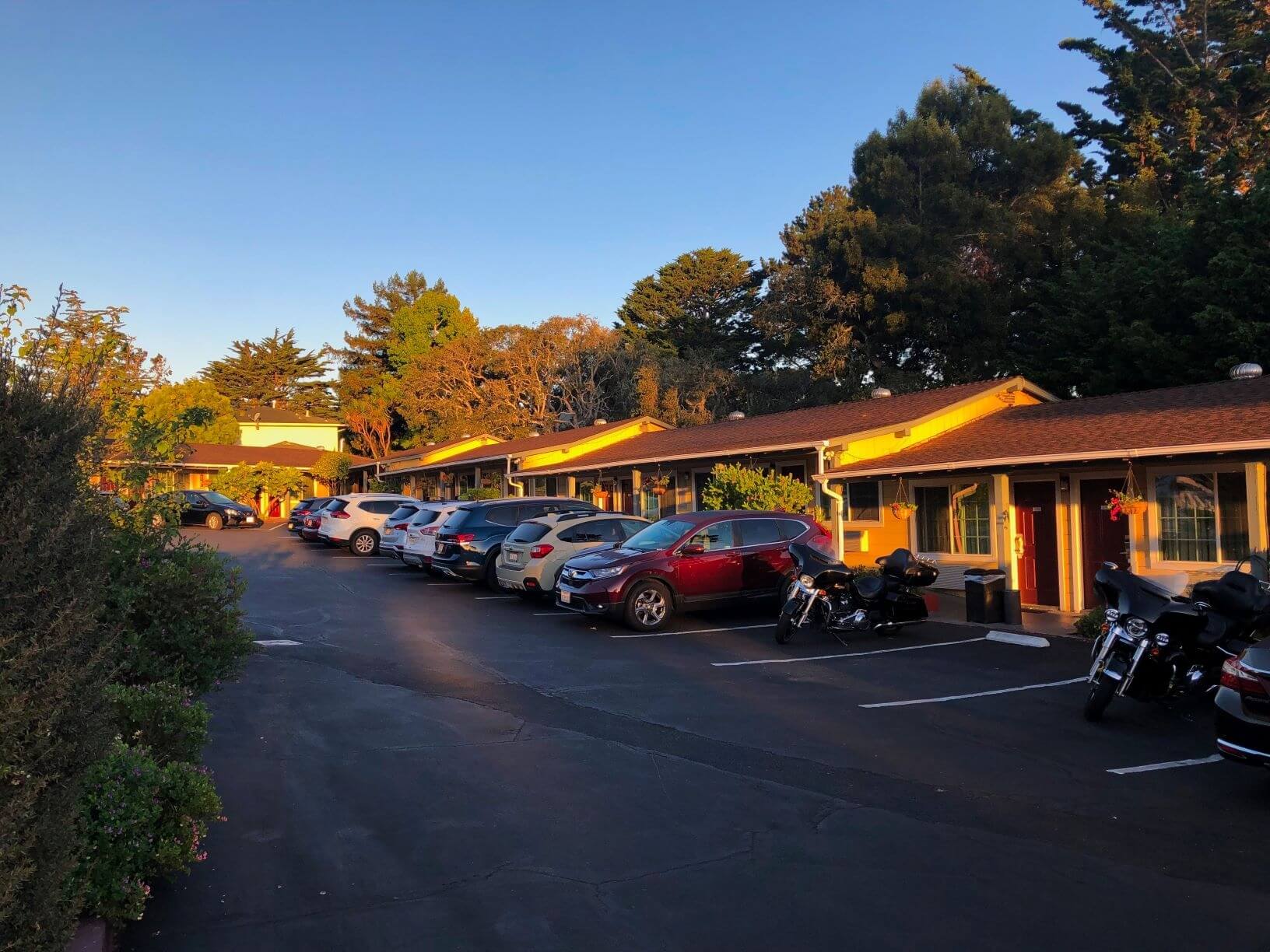 motor hotel at sunrise with vehicles parked in front.