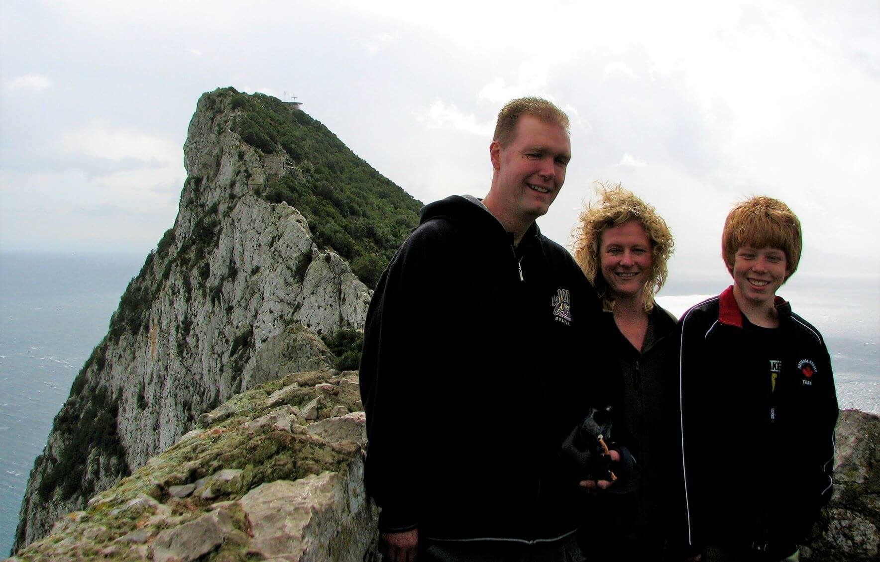 three people, a father, mother and son standing at the top of the Rock of Gibraltar.