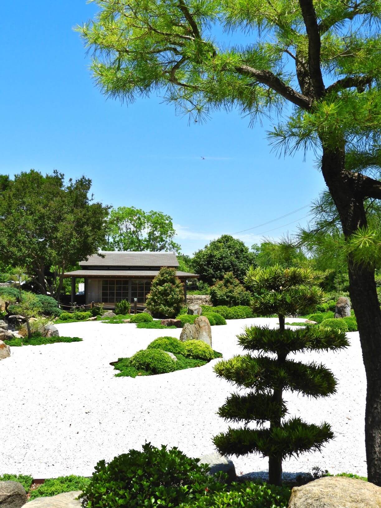 Japanese garden with a pergola, sand, and greenery.