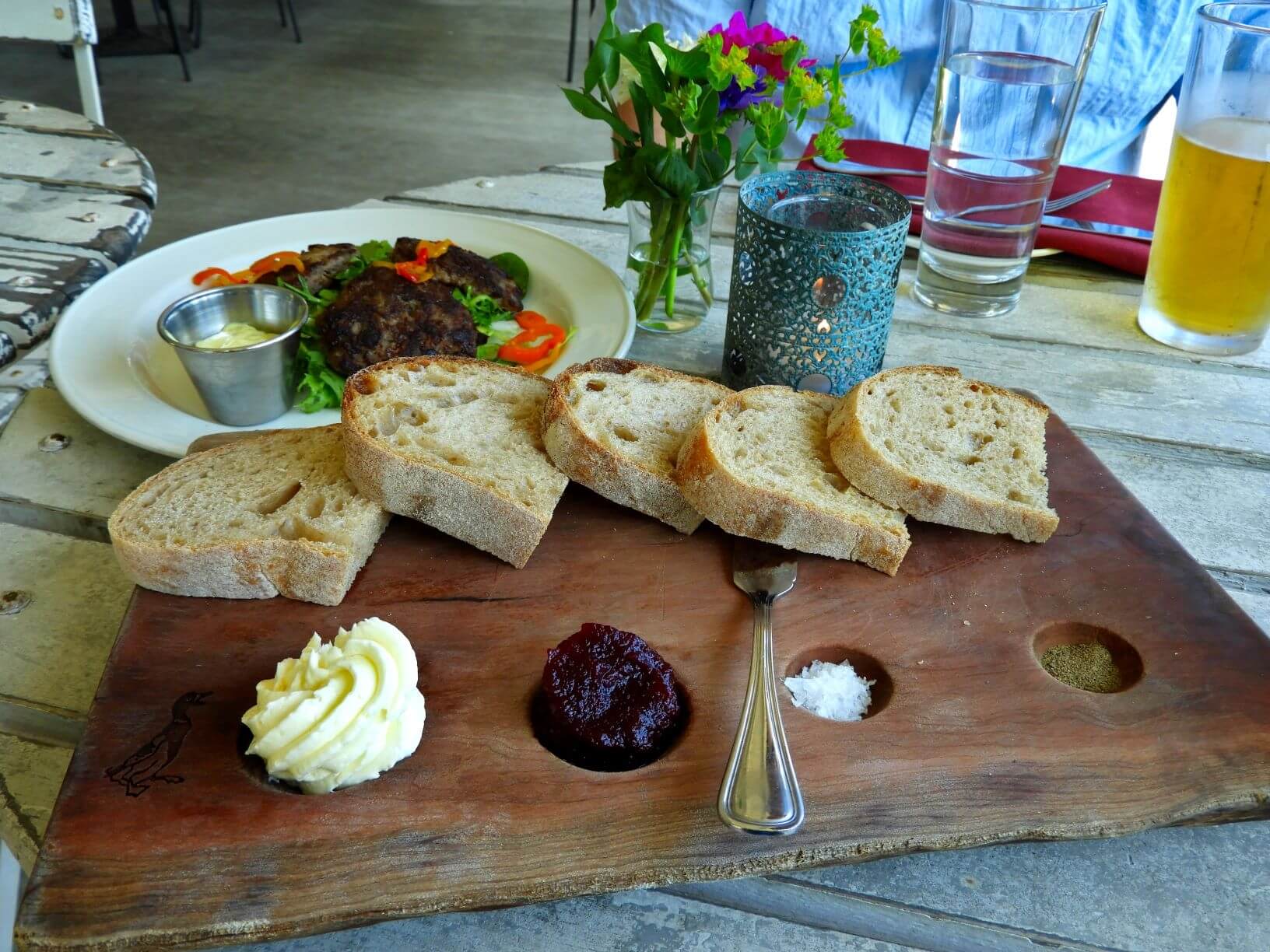 wooden serving plate with bread, butter, beet jam, salt and pepper