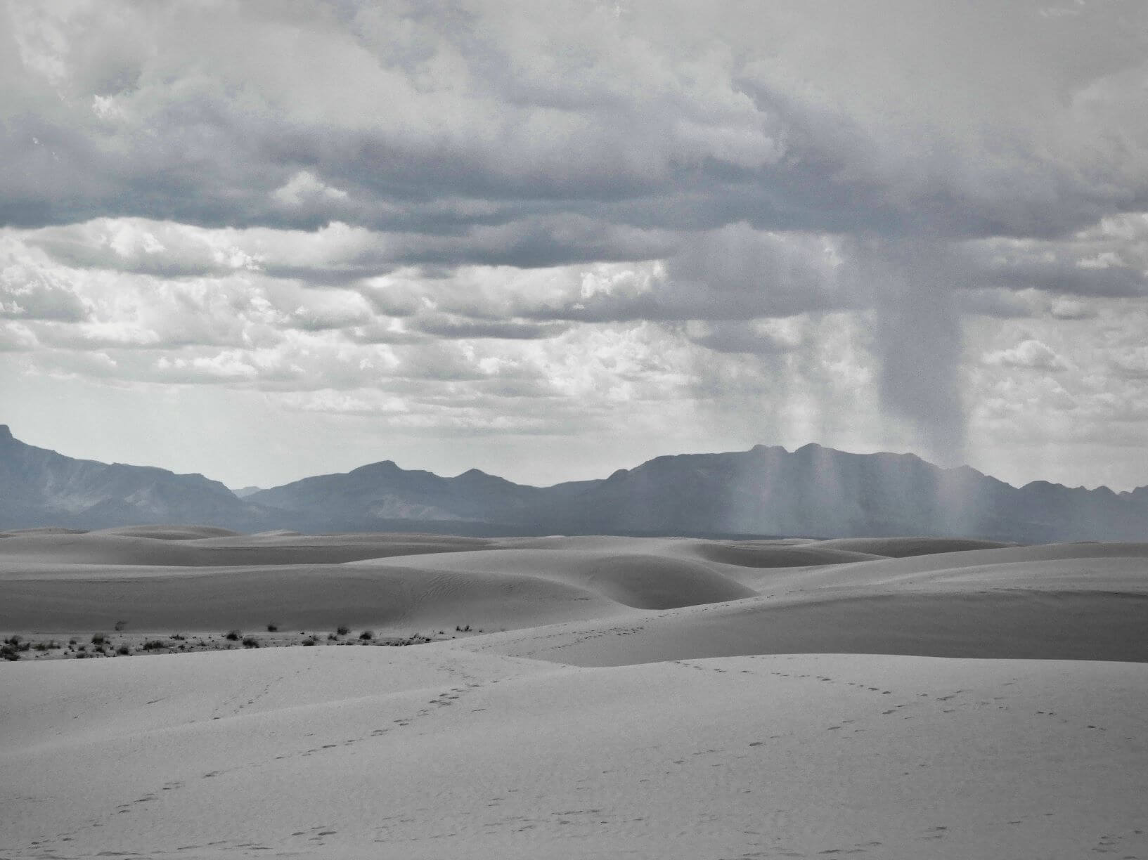 White sand dune fields with mountains and a storm in the distance