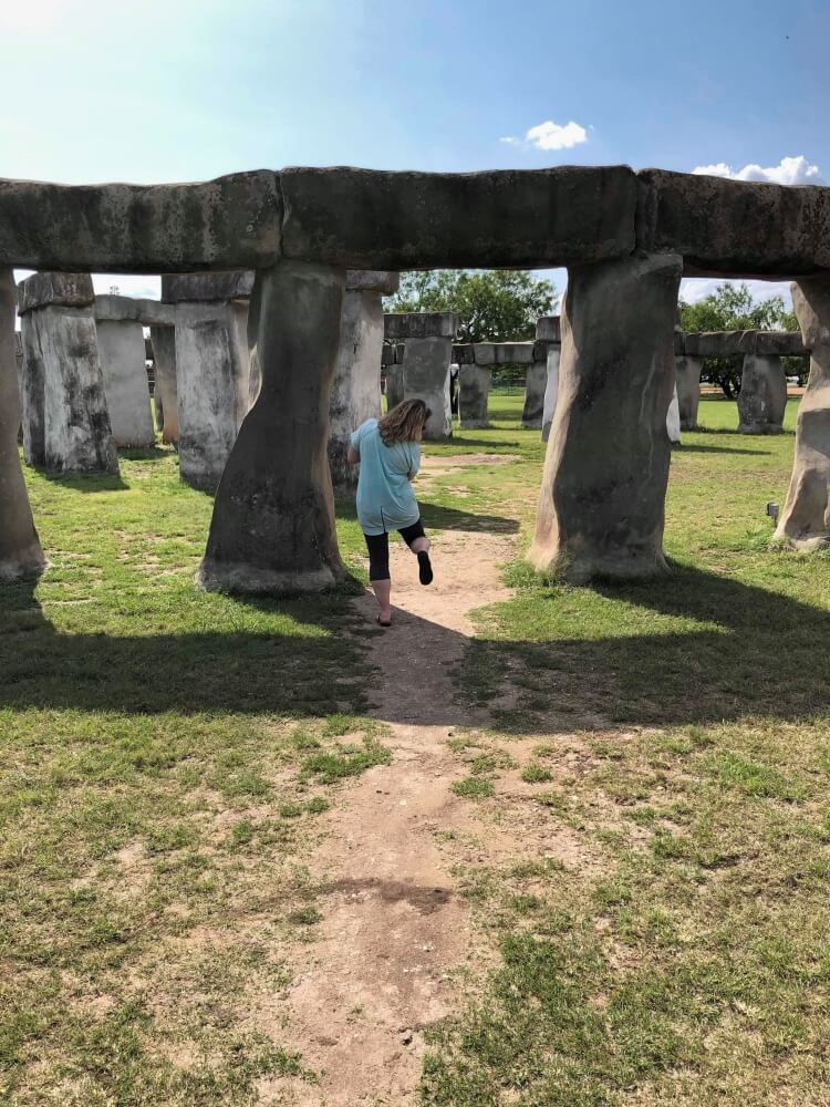 lady walking up to replica stonehenge with a leg lifted
