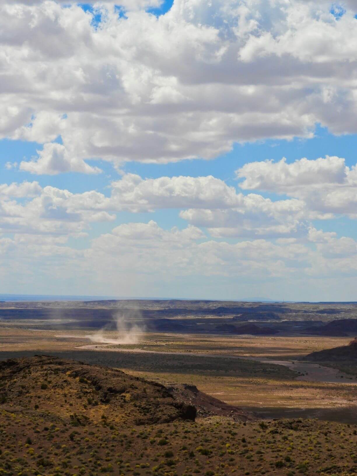 A desert landscape with a small dirt storm in the distance