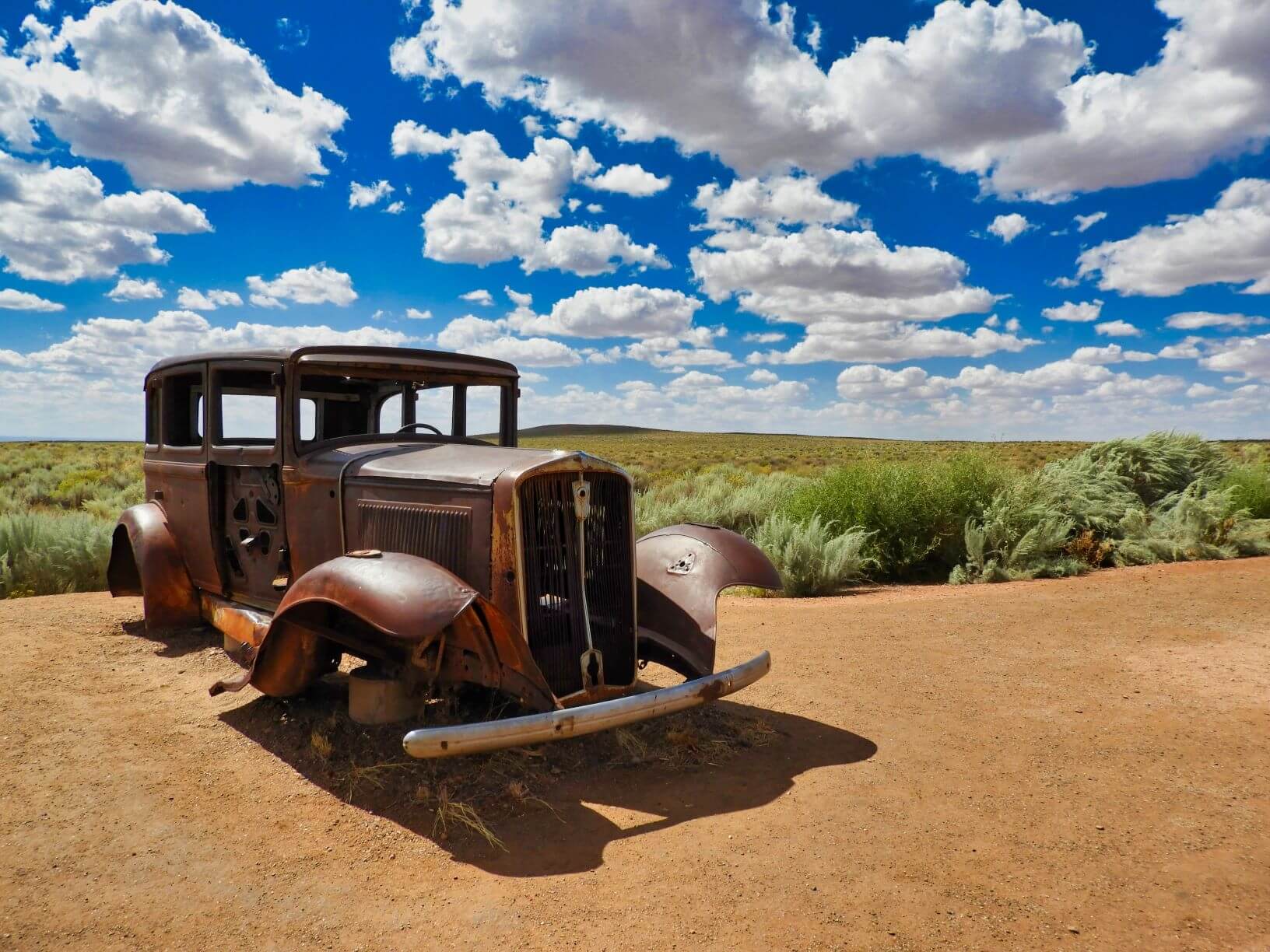 an old car sits abandoned and rusted out in the desert