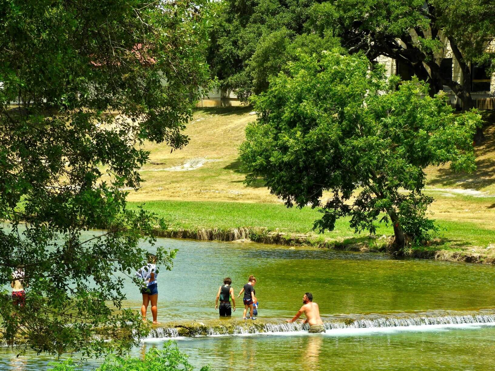 Salado Creek west view with a family and small children wading in the water.
