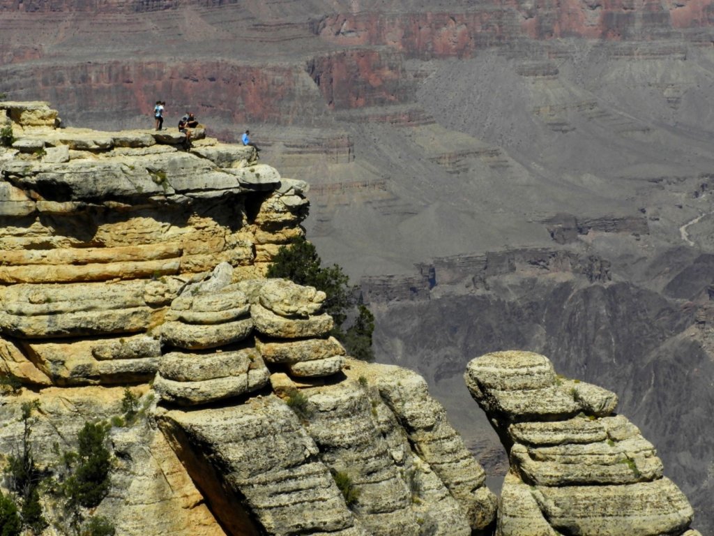 people sitting on the ledge of the grand canyon