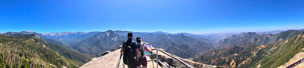two people standing at the top of Moro Rock and looking out over a vast mountain range