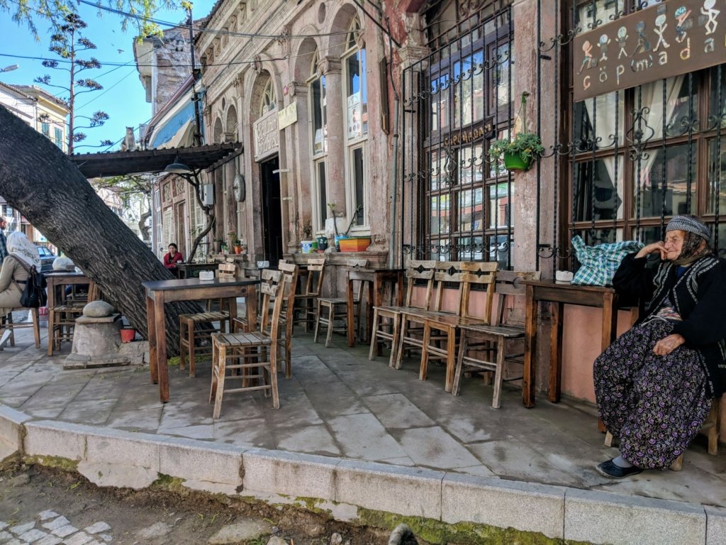 an elderly lady sitting alone on a sidewalk outside a shop.