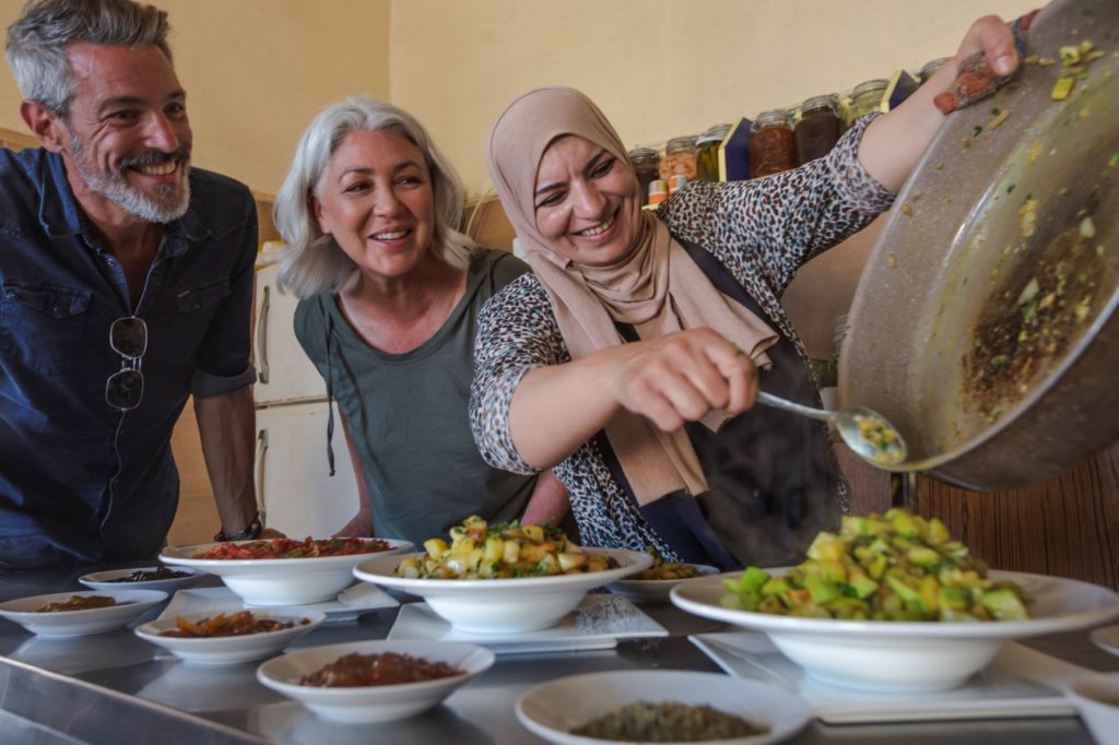 woman dishing out fresh food onto plates as smiling guests look on